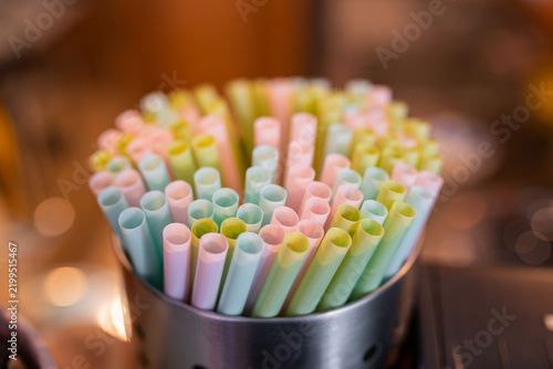 A close-up of colorful straws neatly arranged in a metallic holder, illuminated by warm lighting.