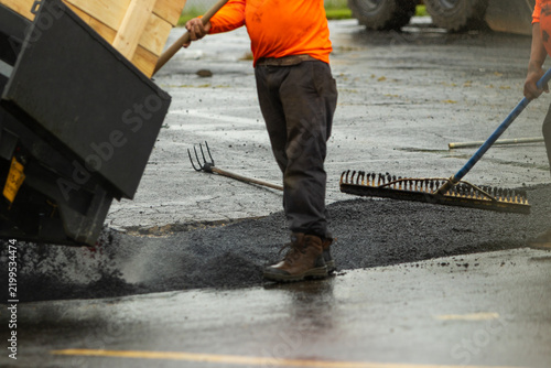 A construction worker standing next to freshly poured asphalt at a work site. 
