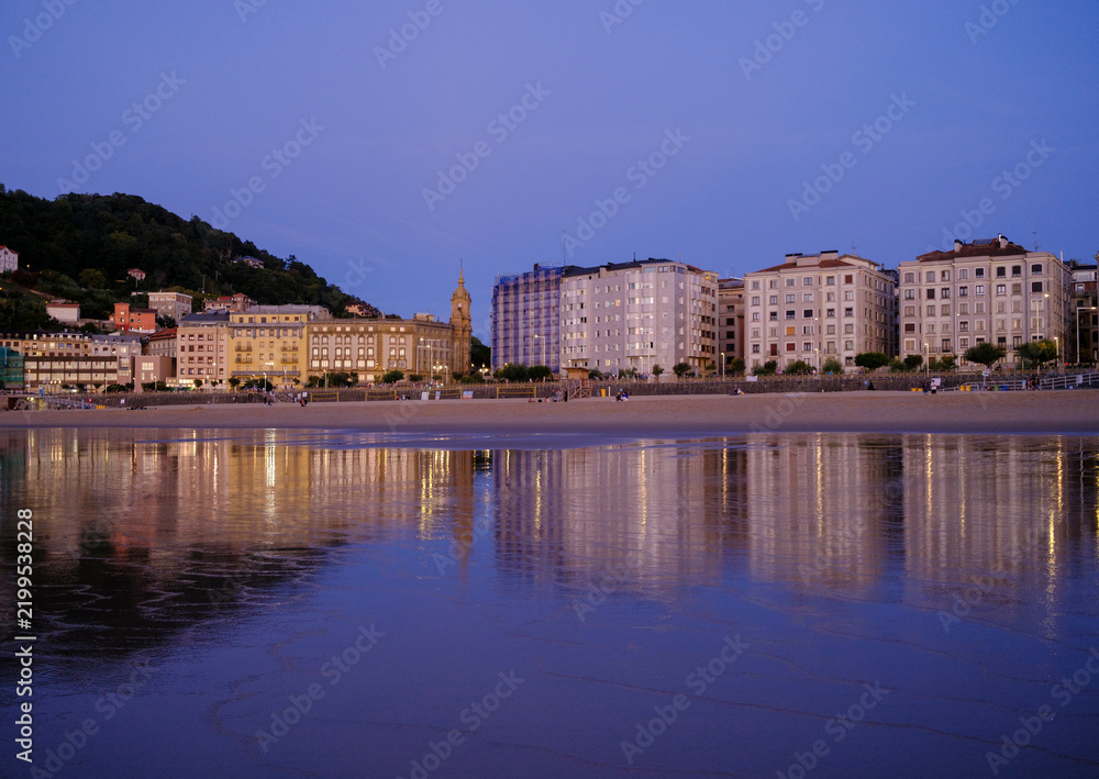 Obraz premium Sunset over Zurriola beach with city reflection on wet sand, San Sebastian, Basque Country, Spain