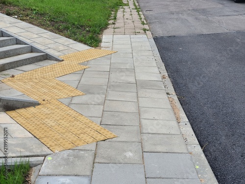 Foto Outdoor urban infrastructure scene showing a paved sidewalk with light grey rectangular stone tiles adjacent to an asphalt road