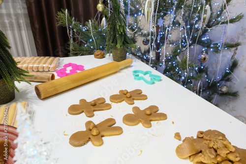Sweet aromas fill the air as bakers roll out gingerbread dough in a cheerful kitchen adorned with a sparkling Christmas tree. Colorful cookie shapes await baking, invoking holiday spirit.