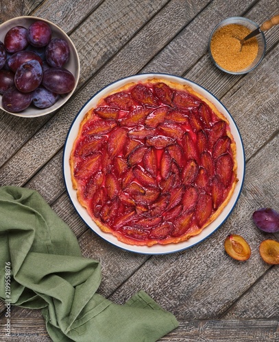 Plum tart on shortcrust pastry on a ceramic plate against a gray wooden background. Plum recipes.