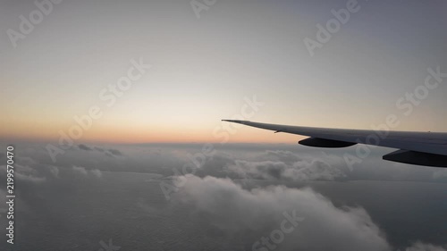 Airplane wing flying above clouds at sunrise