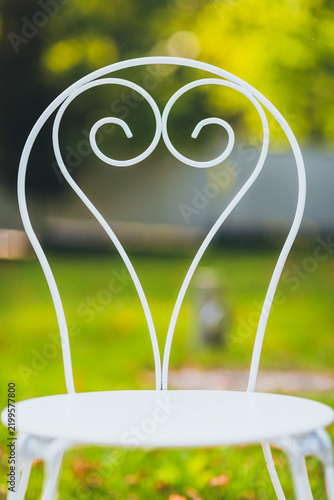 White Decorative Metal Garden Chair with Heart-Shaped Scrollwork and Green Bokeh Background