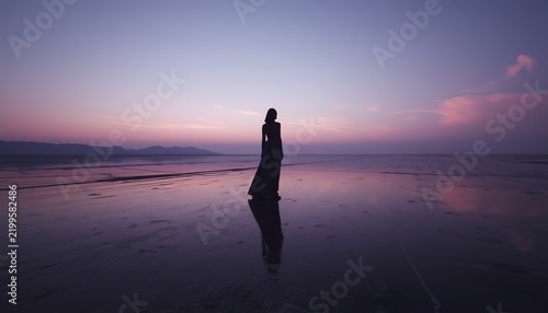 Silhouette of a Woman in a Flowing Gown Standing Alone on a Mirror-Like Salt Flat at Twilight, Reflecting a Surreal Pink and Purple Sky