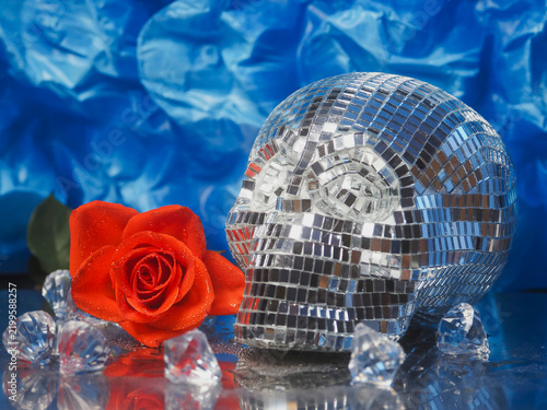 Foto Shiny disco ball skull beside red rose on reflective surface