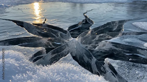 Sunlight reflecting off a frozen lake surface with deep cracks in the thick winter ice