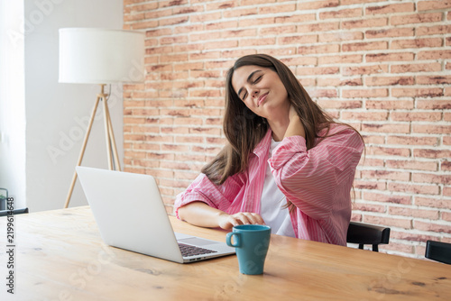 фотографія Young woman feeling neck pain and discomfort while working remotely on a laptop,