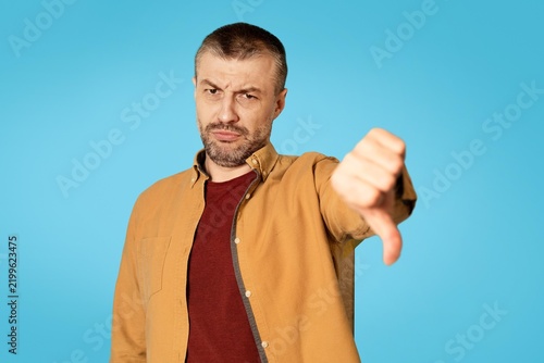 Fotografie Disappointed Caucasian Man Expressing Negative Emotion By Giving Thumbs Down Gesture At Studio Setting