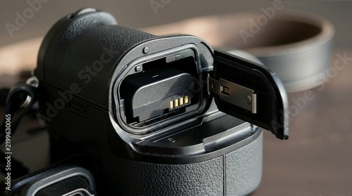 Camera battery inserted into open bottom compartment. Power pack installation inside mirrorless camera grip on wooden surface