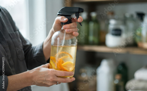 Woman holding homemade natural citrus all-purpose cleaner in glass spray bottle with orange peels