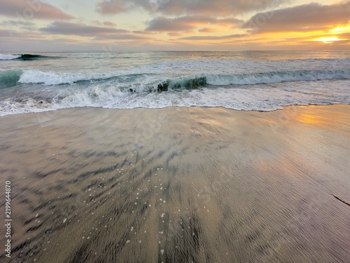 Obraz na płótnie Golden sunset sunlight reflecting off wet beach sand as sea waves wash ashore in Carlsbad, California