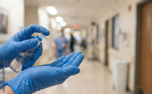 Medical professional wearing blue gloves applying hand sanitizer in a hospital hallway