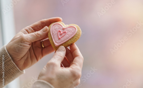 Woman holding a heart-shaped cookie with pink icing representing love and romance for Valentine