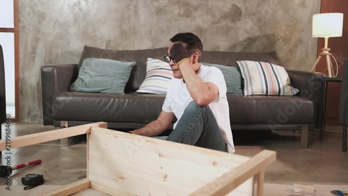 Asian mature man self-assembling carpentry furniture with DIY tools, tightening with screwdriver, tired and resting at living room sofa, home improvement, craft installation, hobby wooden workshop.