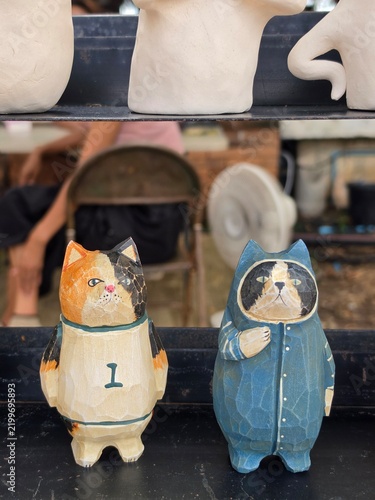 Handmade wooden cat figurines in playful painted outfits stand in a row on a market shelf, each carved with chunky, characterful shapes.