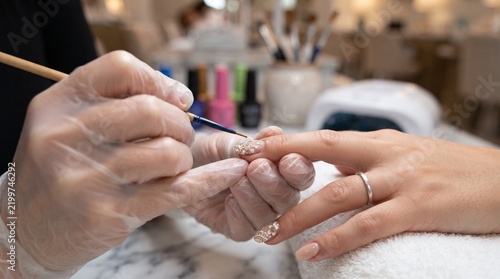 Professional nail technician painting floral patterns on fingernails