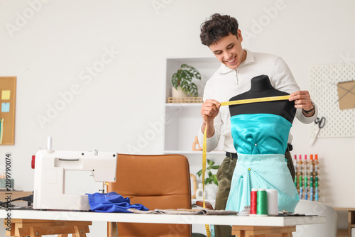 Konstfotografi Young male tailor with sewing machine measuring mannequin in atelier