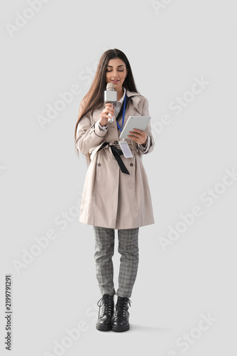 Female journalist with tablet computer and microphone on light background