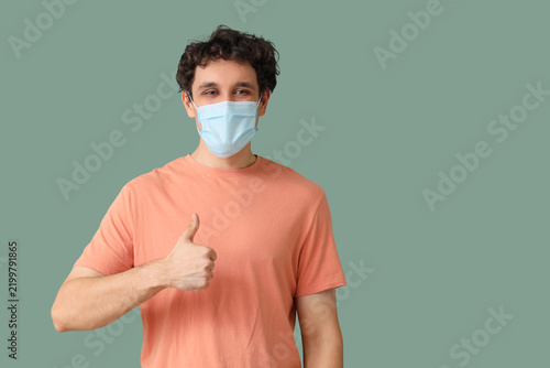 Young man in medical mask showing thumb-up on green background. Immunity concept