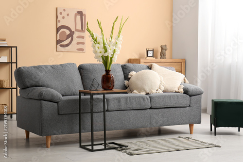 Comfortable grey sofa, table and vase with beautiful white gladiolus flowers ...
