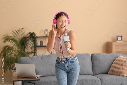 Beautiful young happy Asian woman in headphones with microphone singing while...