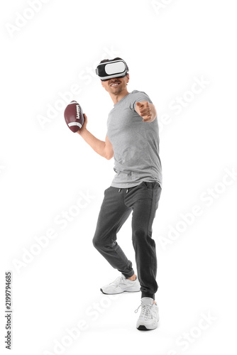 Sporty young man in VR glasses with rugby ball on white background