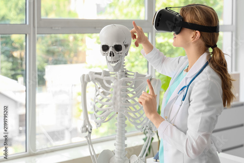 Female doctor in VR glasses with human skeleton model at hospital