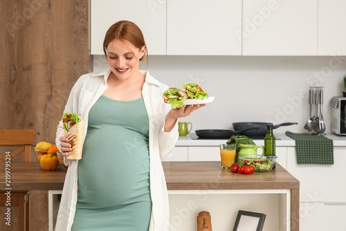 Young pregnant woman with tasty doner kebab in kitchen