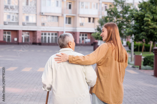 Senior woman with stick and caregiver hugging outdoors, back view