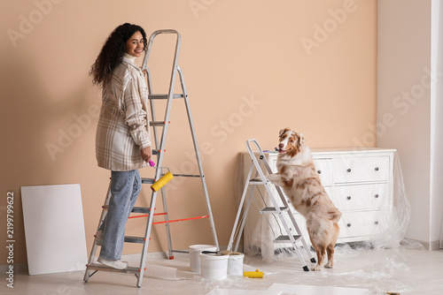 Happy female African-American painter with roller and cute Australian Shepher...