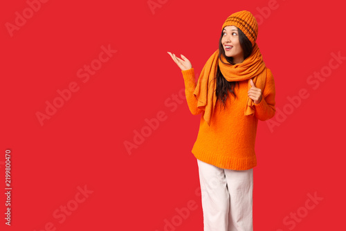 Beautiful young Asian woman in knitted hat and scarf pointing at something on...