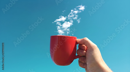 Hand Holding Red Coffee Mug with Cloud Shaped Steam Against Clear Blue Sky, Creative Minimal Concept