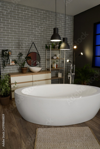 Interior of dark bathroom with bathtub, sink and glowing lamps in evening