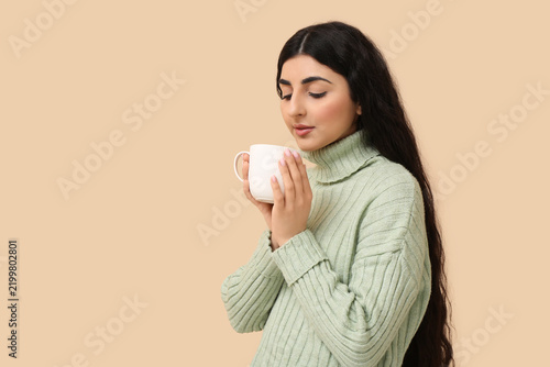 Beautiful young woman with cup of hot tea on beige background