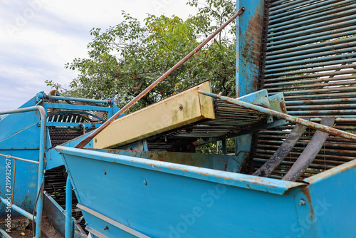 Foto Blue metal potato digger with an inclined conveyor and a hopper is prepared for harvesting