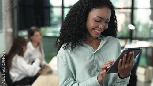 Smiling businesswoman using digital tablet in modern office, working on online project, reviewing business data and enjoying productive mobile technology for professional workplace tasks.