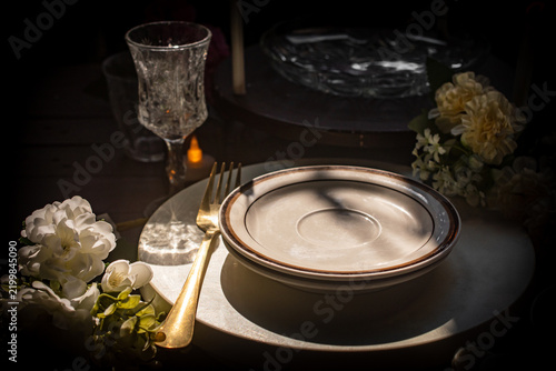 Spooky Halloween candlelight dinner table setting with burning candles, empty plate, crystal glass, and dark vintage atmosphere for a creepy gothic party or haunted mansion concept. 

