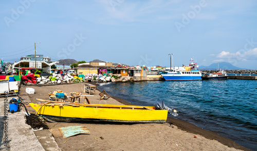 Yellow motorboat resting on the volcanic sand beach along Basseterre harbor in Saint Kitts with ferries docked in the background.