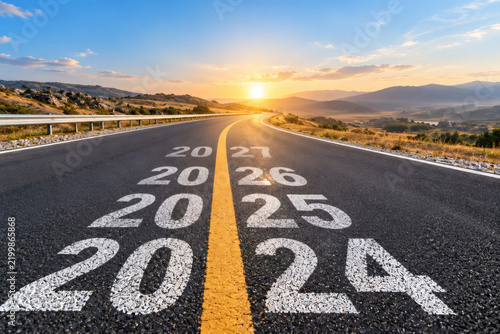 Open road with years 2024 to 2027 painted on asphalt symbolizing future progress and journey towards new year goals with sunset in the background