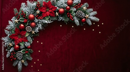 Festive christmas wreath arrangement with poinsettia flowers and decorative ornaments on a dark red velvet background