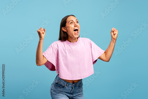 Young woman celebrating success with excitement and triumph isolated on blue background