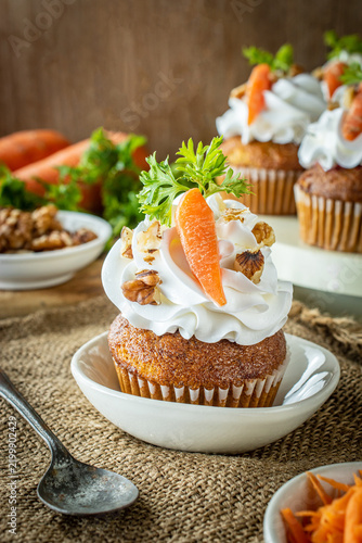 Freshly baked carrot cake cupcakes topped with smooth buttercream, walnuts, and fresh parsley, served on a rustic burlap tablecloth alongside raw carrots