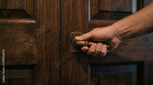 Man opening ancient wooden door by turning the brass handle knob
