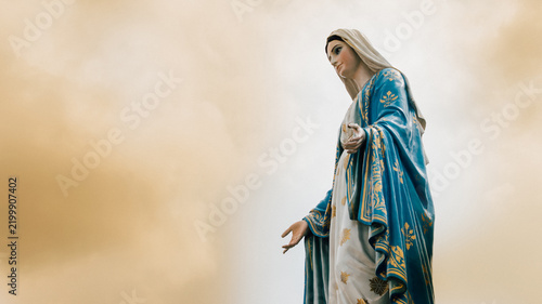 Obraz na plátně Virgin Mary statue blue white robes against soft neutral background generous cop