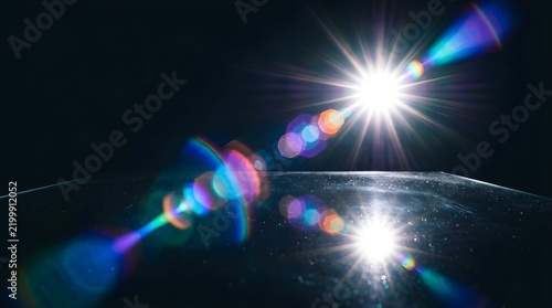Anamorphic lens flare with rainbow light leaks, cinematic sun star reflection on dark surface, futuristic optical glow for overlay effects