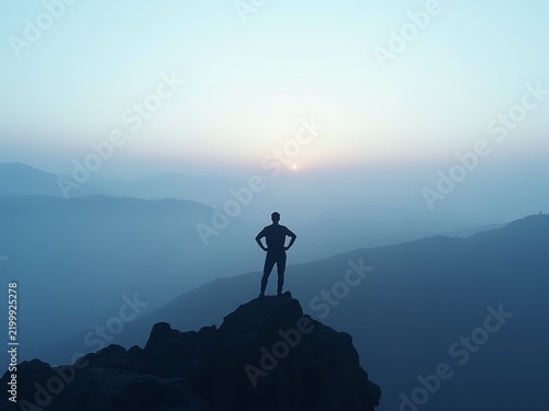 A lone figure stands triumphantly in silhouette on a rugged peak, gazing at a misty landscape under a soft dawn sky of blue, lavender, and gold.
