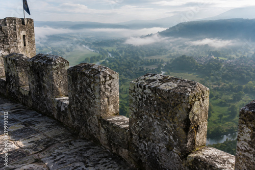 Medieval stone battlement with merlons and crenels overlooking misty valley, historic fortification