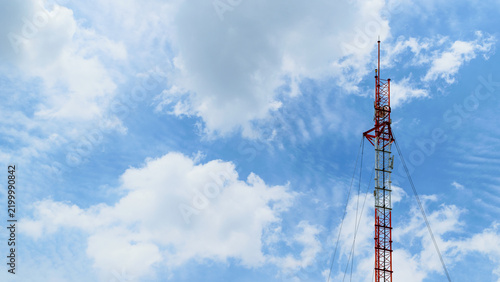 Tall telecommunication tower rising against bright blue sky white clouds representing wireless communication broadcasting network infrastructure