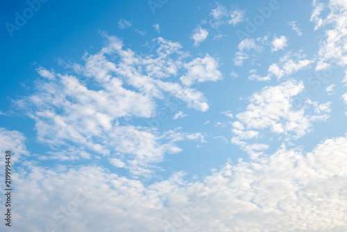 Bright blue sky background filled with scattered soft white cumulus and cirrus clouds on a clear sunny day, natural skyscape asset with open space.